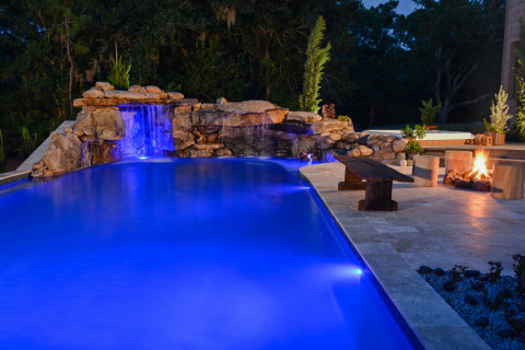 A natural lagoon pool glows with underwater and outdoor lighting along with the warm glow from a pool side fire pit.