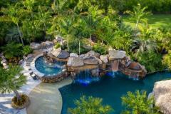 Aerial perspective of a waterslide winding into a lagoon-style pool with tropical trees. Aerial perspective of a waterslide winding into a lagoon-style pool with tropical trees.
