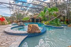 Waterslide framed by vibrant tropical plants and stonework in a custom outdoor pool setting Waterslide framed by vibrant tropical plants and stonework in a custom outdoor pool setting