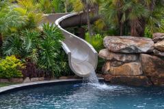 Close-up of a backyard waterslide with natural stone and lush greenery . Close-up of a backyard waterslide with natural stone and lush greenery .