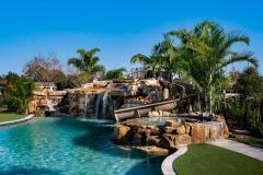 Resort-style backyard pool featuring a curved waterslide integrated into rock formations. Resort-style backyard pool featuring a curved waterslide integrated into rock formations.