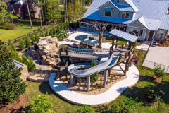 High vantage view of a custom waterslide spiraling into a lagoon-style pool design. High vantage view of a custom waterslide spiraling into a lagoon-style pool design.