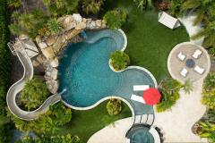 Aerial perspective of a waterslide winding into a lagoon-style pool with tropical trees. Aerial perspective of a waterslide winding into a lagoon-style pool with tropical trees.