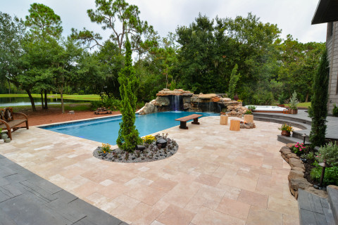 Looking out over the large travertine deck area of a great natural outdoor living space with a northern rock waterfall