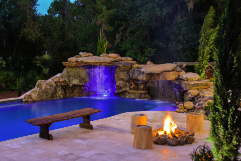 A natural wood bench sits by the edge of this real rock lagoon waterfall with a fire pit