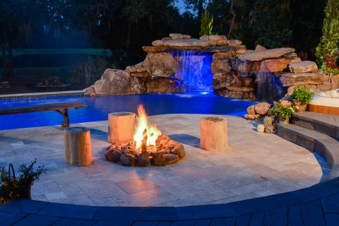 A blazing fire pit warms the evening air in a large outdoor living area complete with natural stone lagoon pool