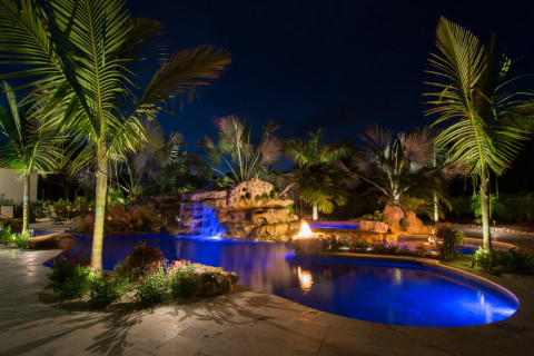 Natural lagoon pool sundeck wading area at night with fire pits and stone grotto